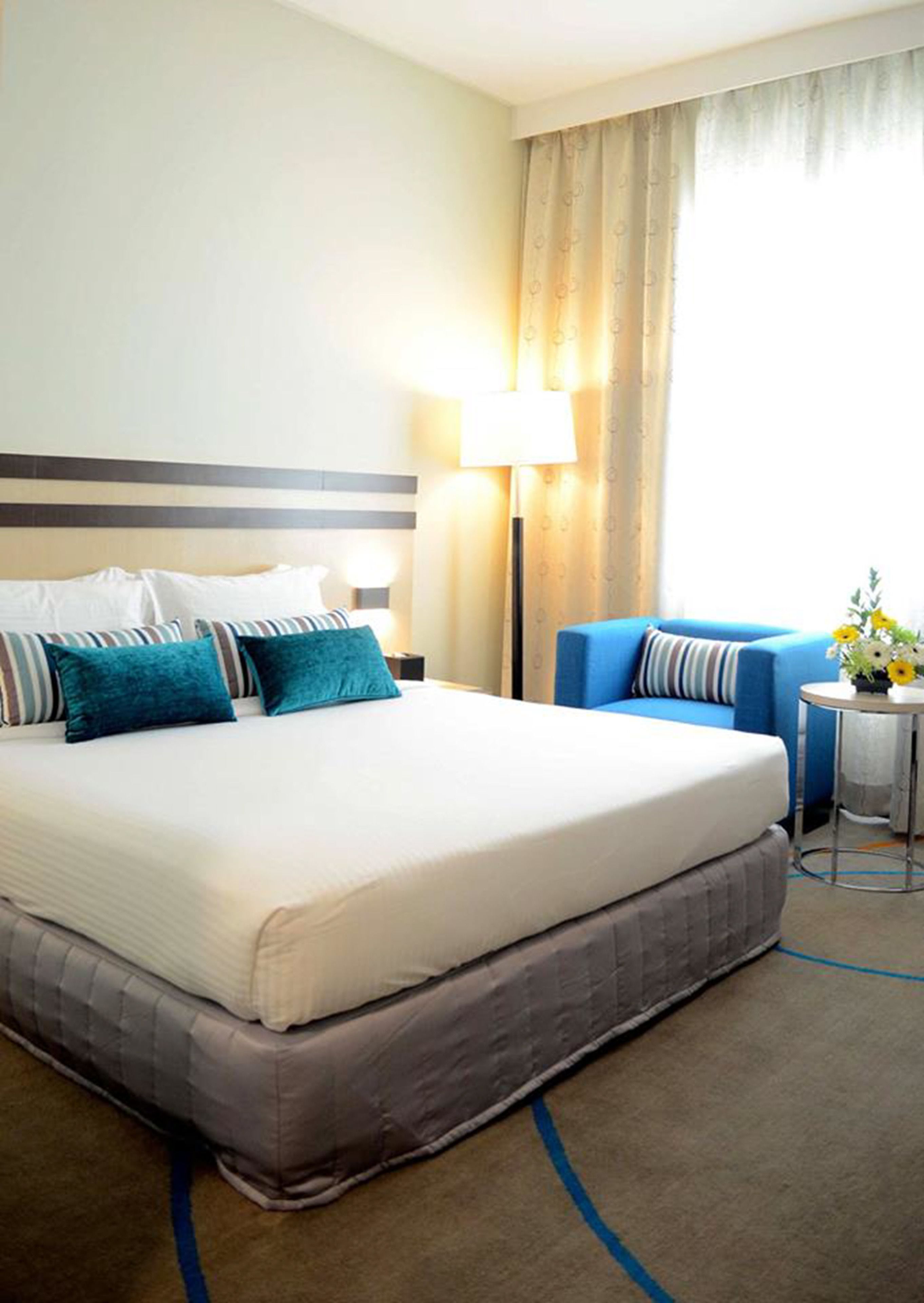 Camera d'albergo con un letto grande, una lampada da comodino, un tavolino con fiori e una poltrona blu.