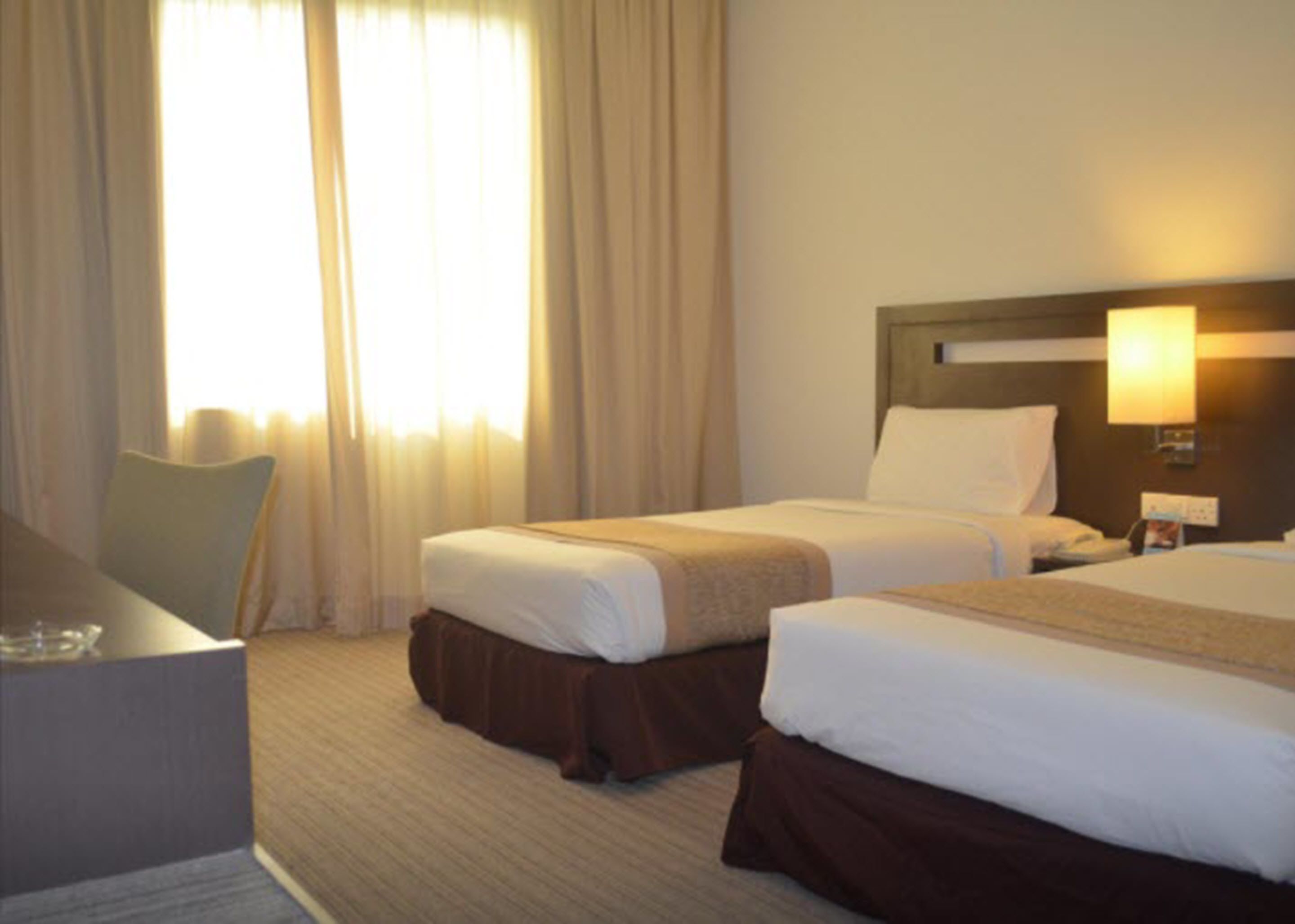 A hotel room with two beds, a desk, and a window with curtains.