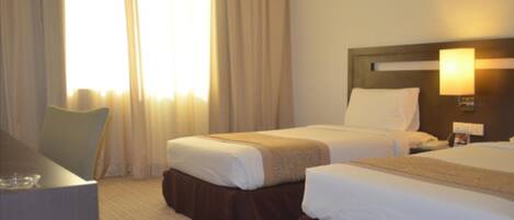 A hotel room with two beds, a desk, and a window with curtains.