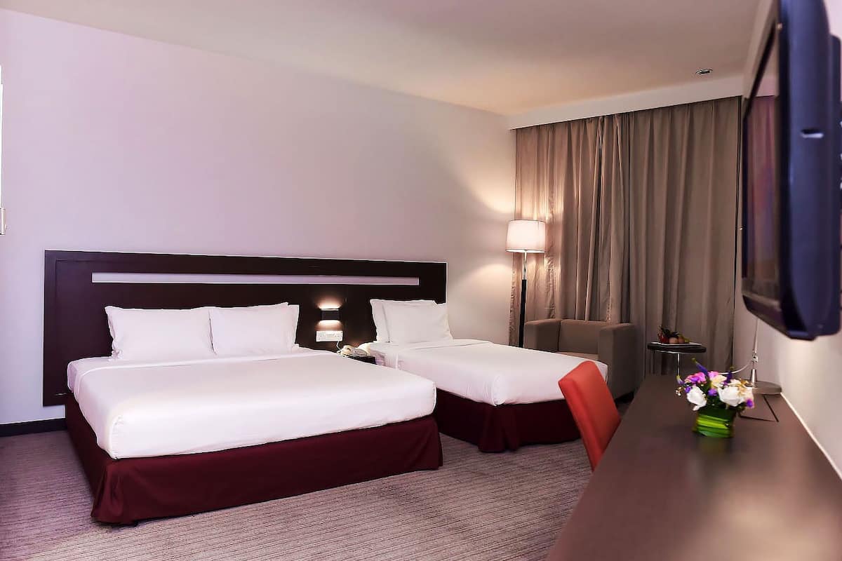 A hotel room with two beds, a desk, a chair, a TV, and a lamp.
