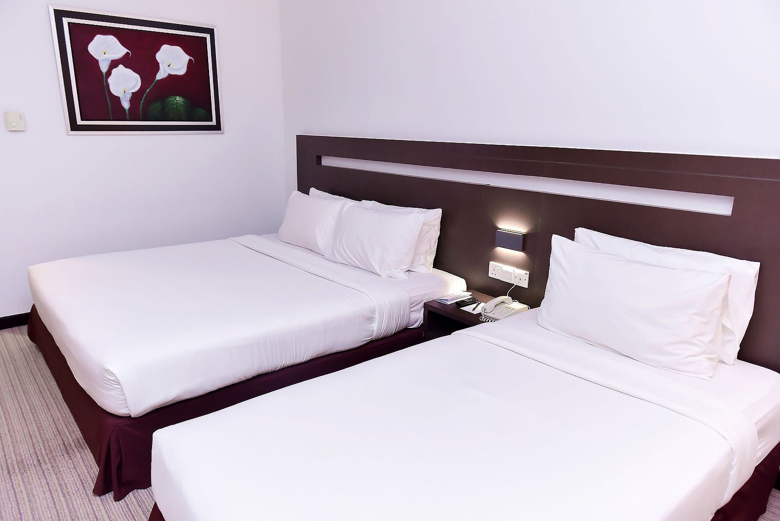 Une chambre d’hôtel avec deux lits simples, une table de chevet avec un téléphone et une œuvre d’art encadrée au mur.