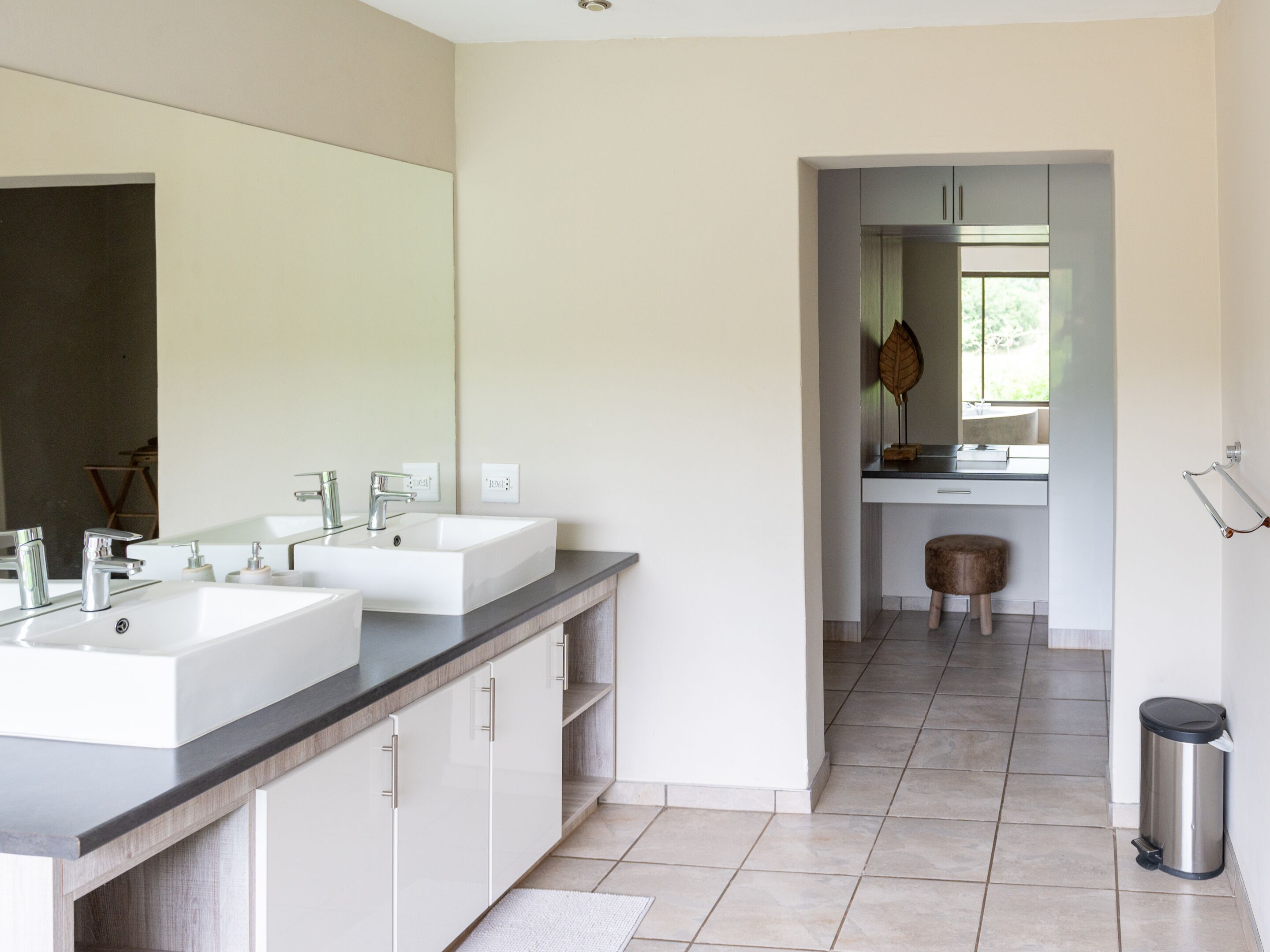 A modern bathroom with two sinks, a large mirror, and a wooden stool.