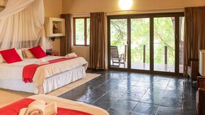 Een hotelkamer met een groot bed, een kleiner bed en een balkon met uitzicht op bomen.