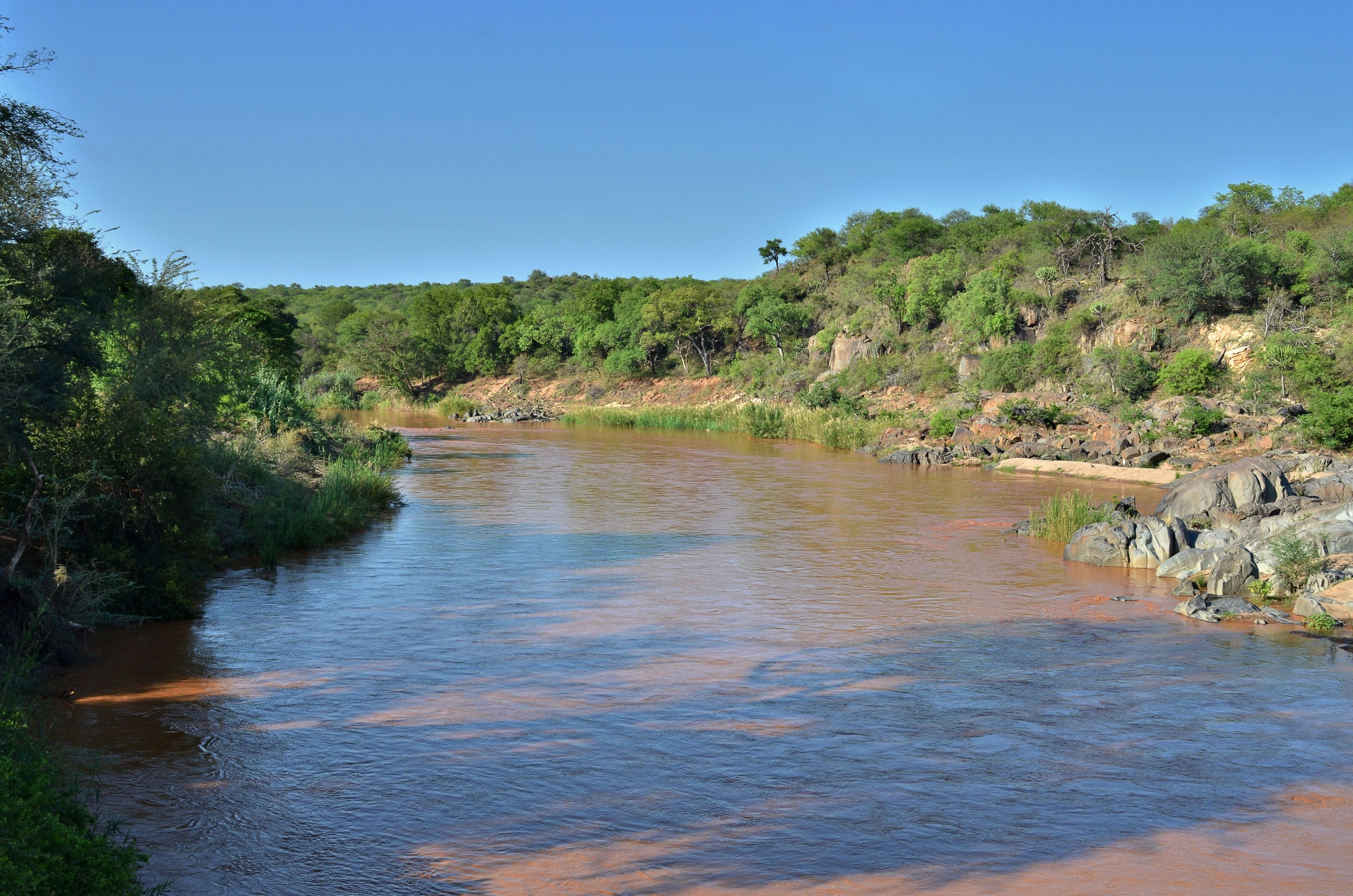 A river flowing through a natural landscape with dense greenery and rocky terrain.