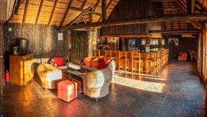 Een ruime kamer met een hoge kap en rieten dak, met een bar en een zithoek met rieten meubels.
