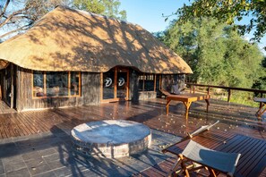 Un bâtiment à toit de chaume doté d’une terrasse en bois, d’un foyer et de sièges extérieurs.