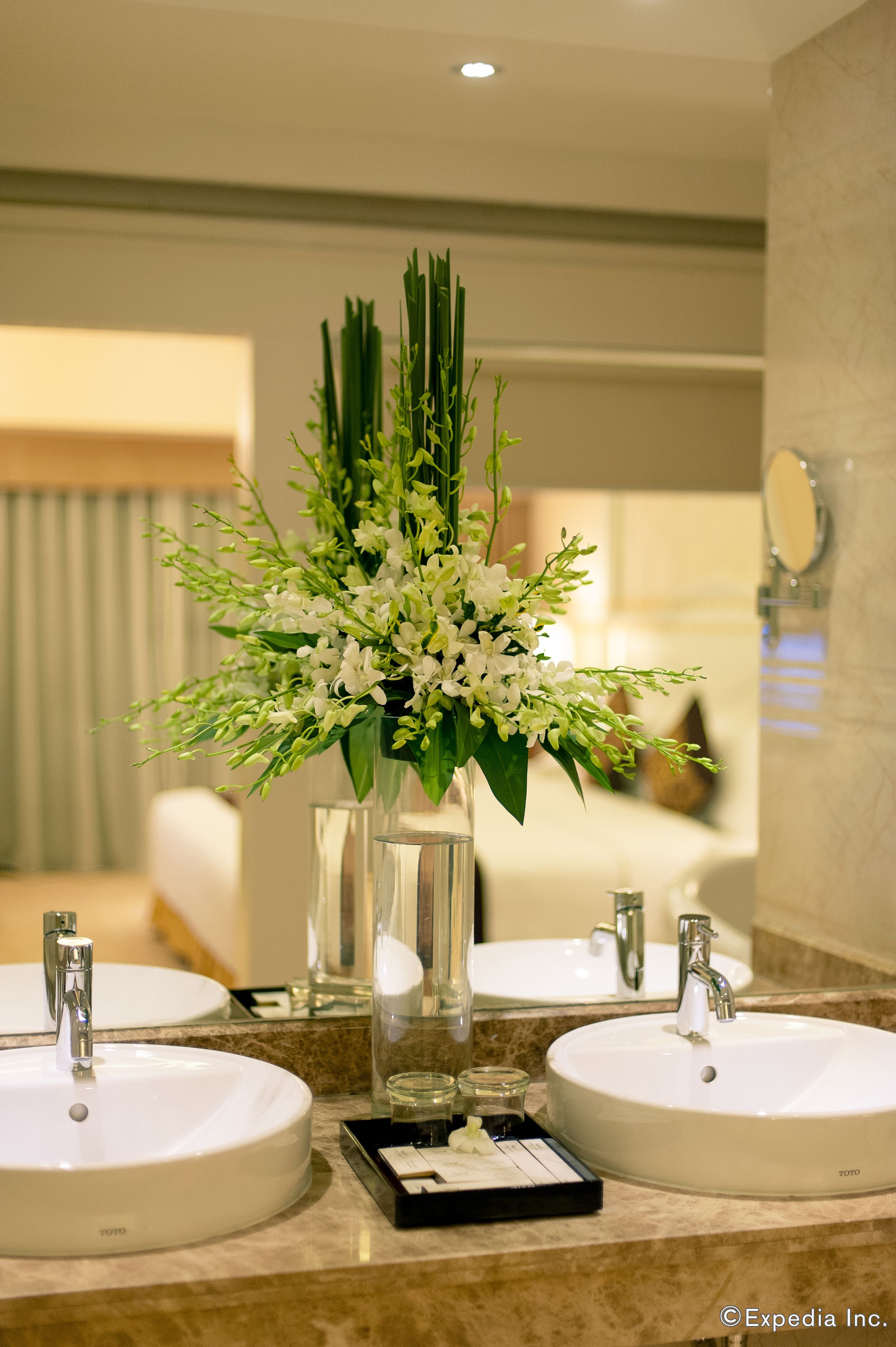 A bathroom with two sinks, a mirror, and a vase with white flowers.