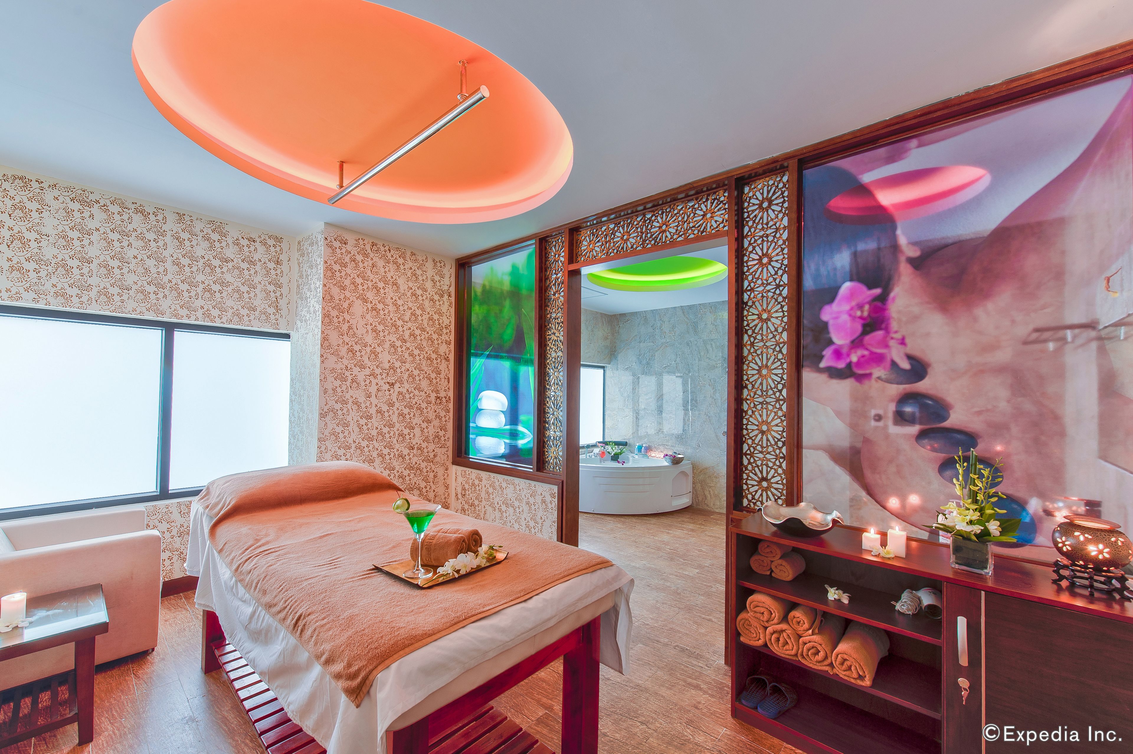 Un spa moderno con una cama, una camilla de masaje, un sillón de masajes, un ventanal grande y un espejo decorativo.