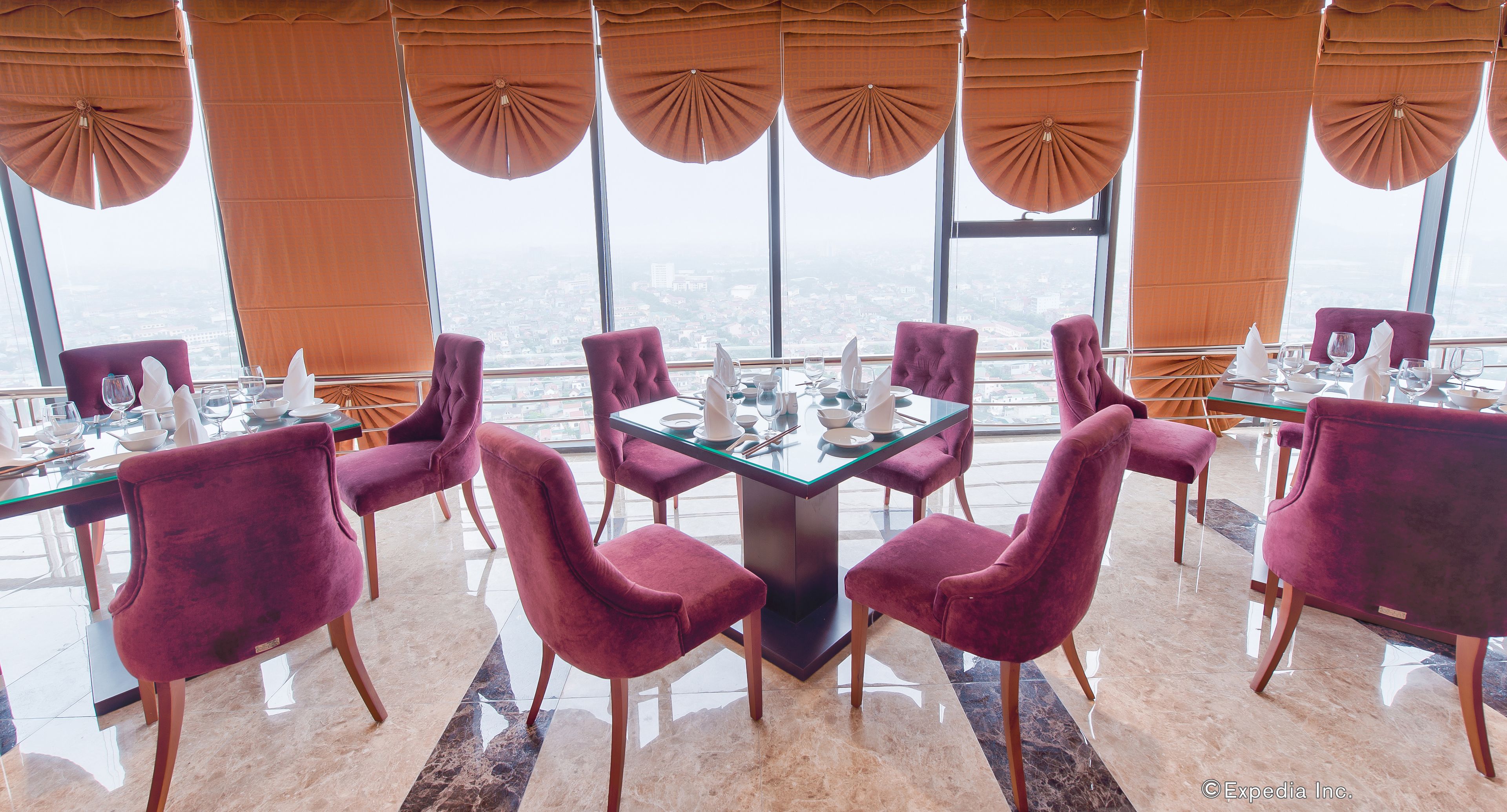Un coin repas avec une table en verre entourée de chaises violettes, de grandes fenêtres avec des rideaux et une vue sur la ville.