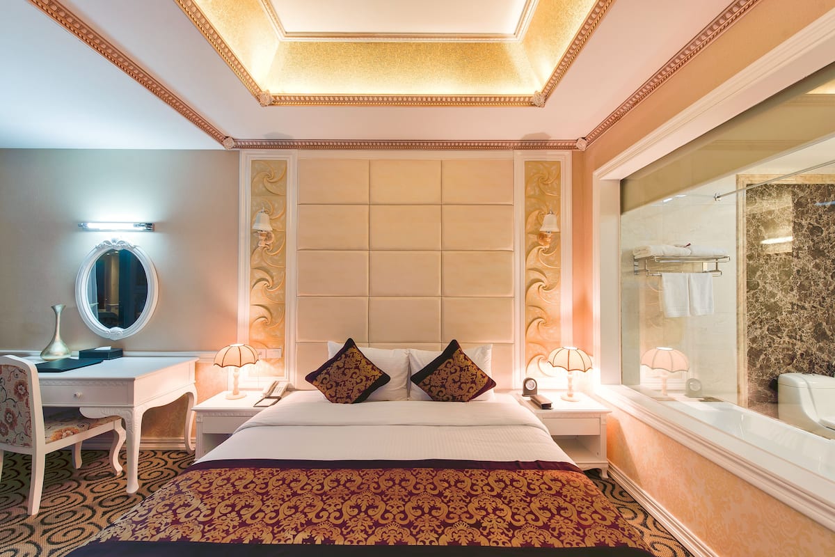 Een hotelkamer met een groot bed, een bureau met spiegel, twee bedlampjes en een grote spiegel aan de muur.