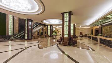 A spacious lobby with a marble floor, escalators, seating areas, and a reception desk.