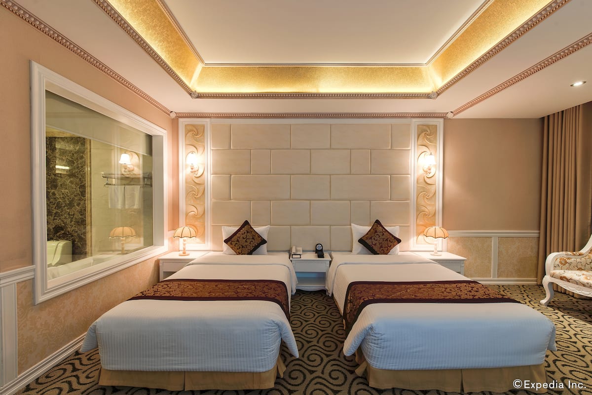 Een hotelkamer met twee bedden, een grote spiegel, een hoofdeinde met ingebouwde verlichting en een kamerbreed tapijt met dessin.