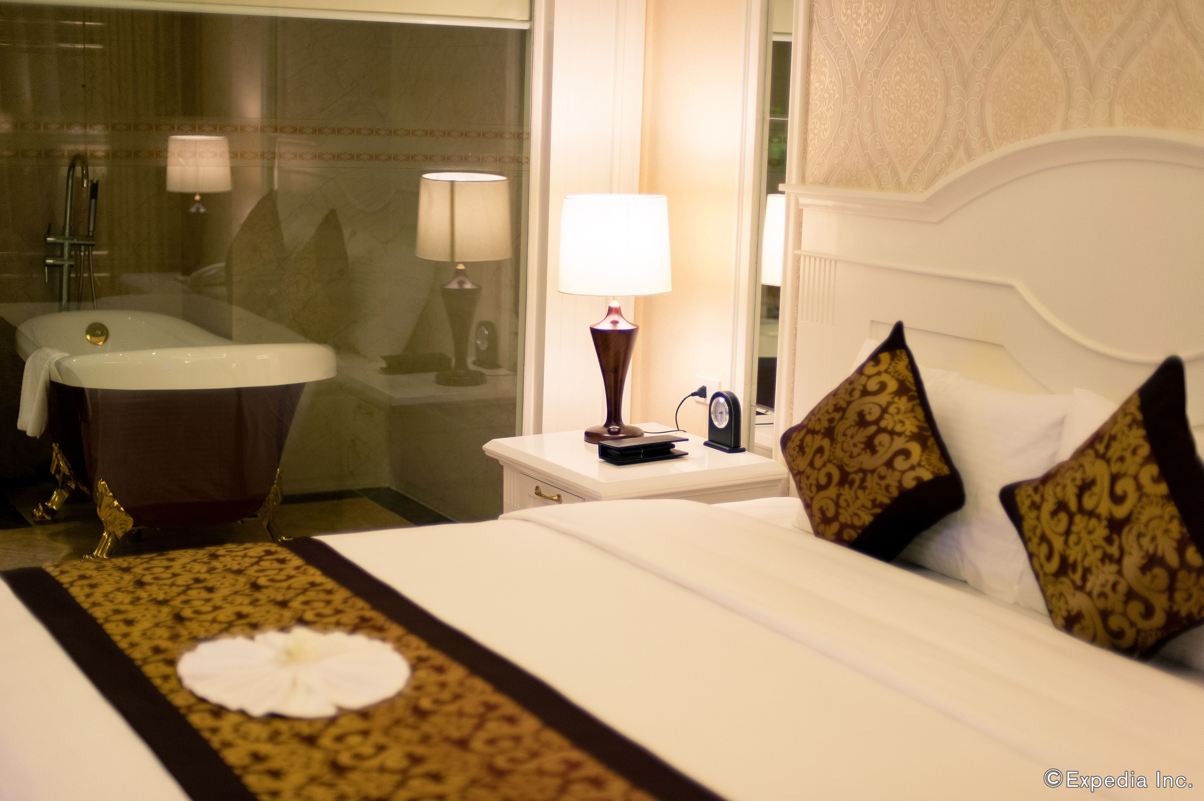 Een hotelkamer met een groot bed, een nachtkastje met lamp, een badkamer met bad en een spiegel.