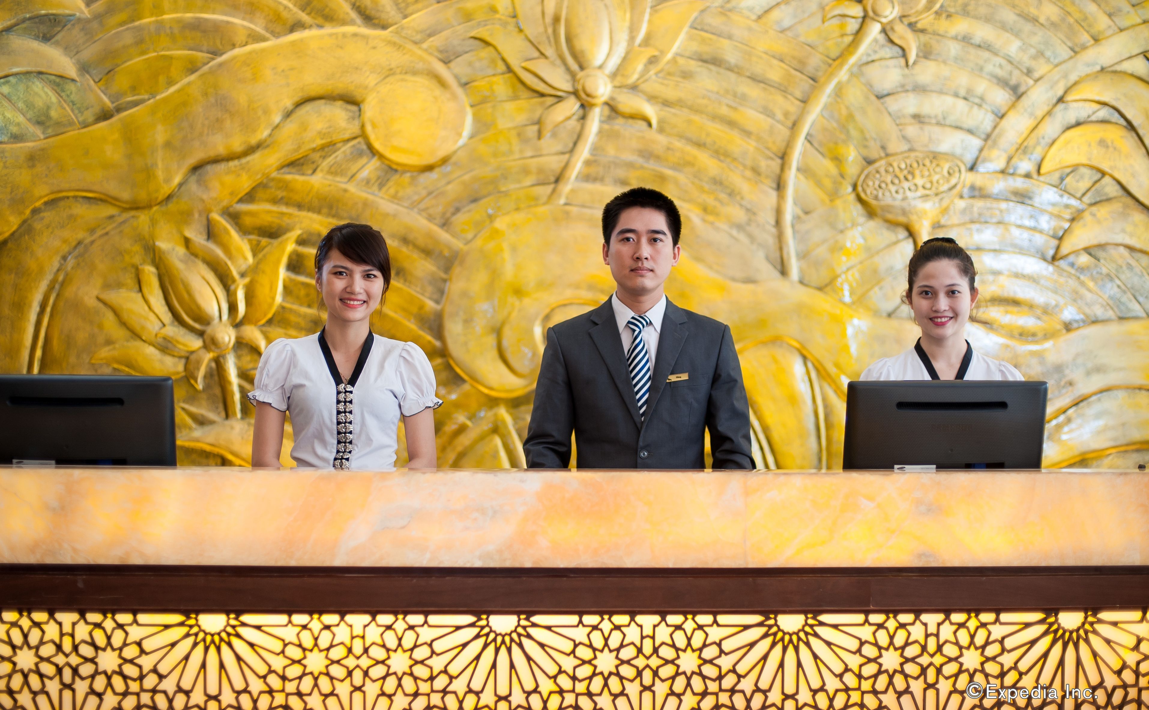 Recepcionistas en el mostrador de un hotel, con una pared dorada decorativa de fondo.