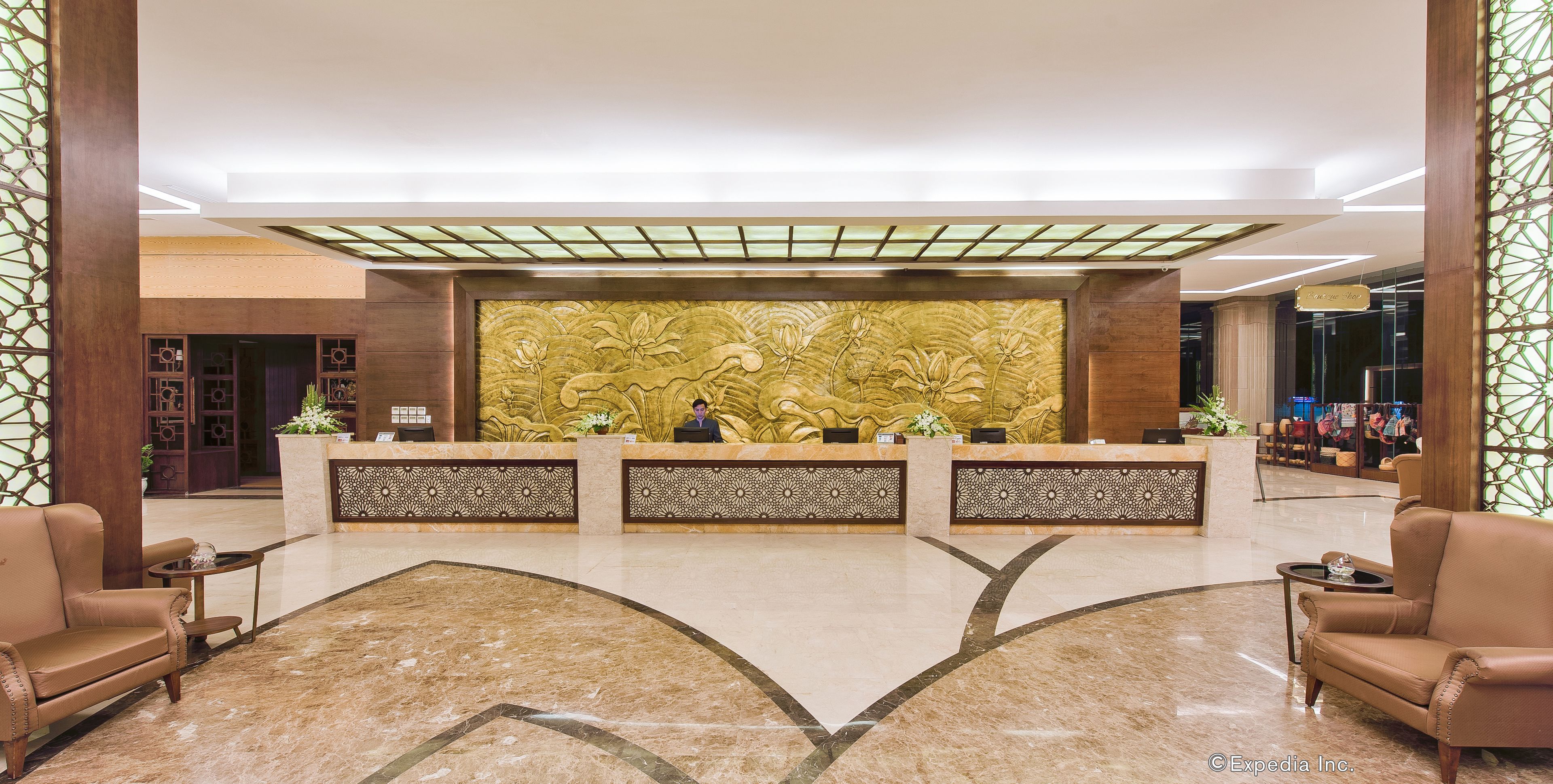 A hotel reception area with a marble floor, two reception desks, and a large decorative wall.