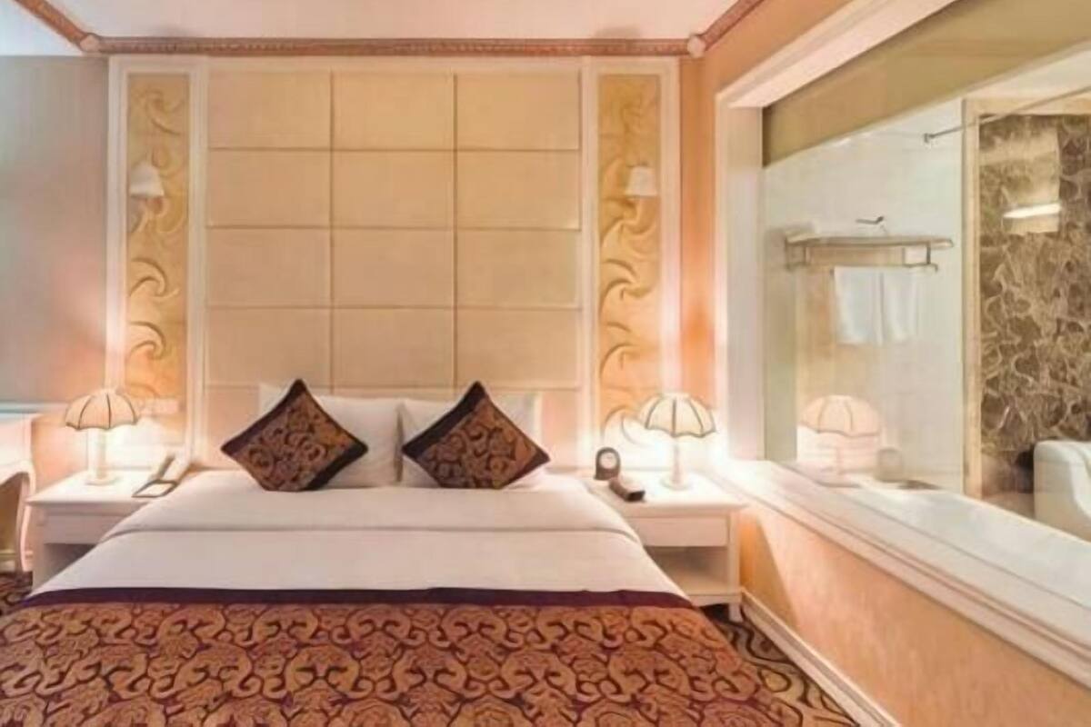 Een hotelkamer met een groot bed, twee nachtkastjes, een grote spiegel en uitzicht op de badkamer.