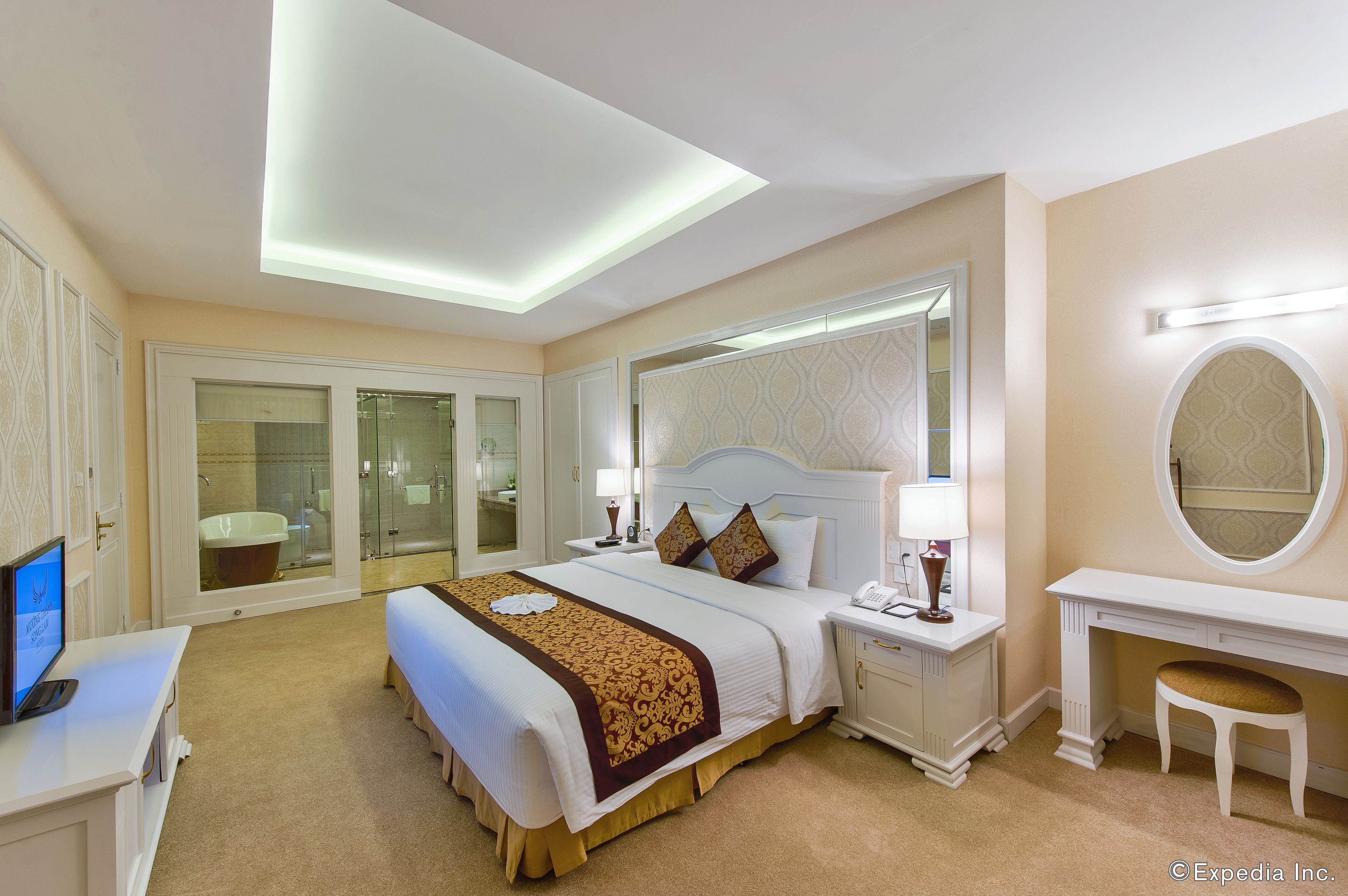 A hotel room with a bed, bedside tables, a desk, a chair, a mirror, and a bathroom with a bathtub and shower.