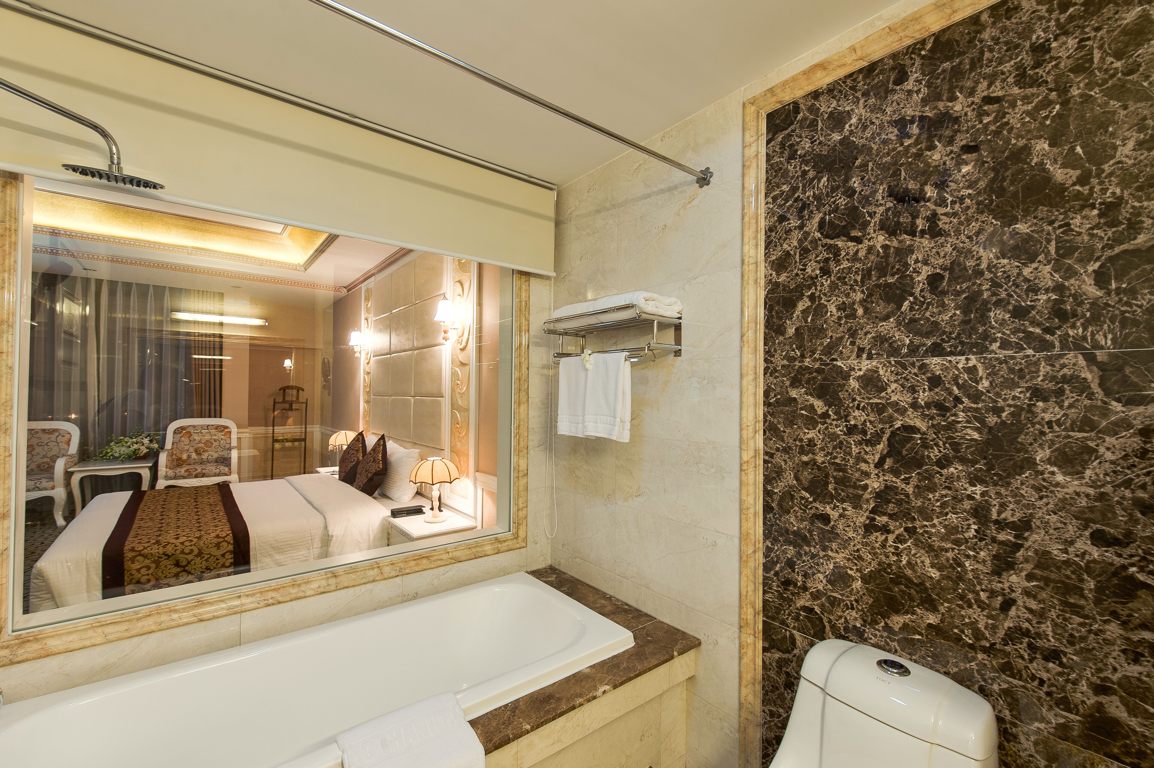 Un baño con un espejo grande, una bañera, un inodoro y un perchero para toallas.
