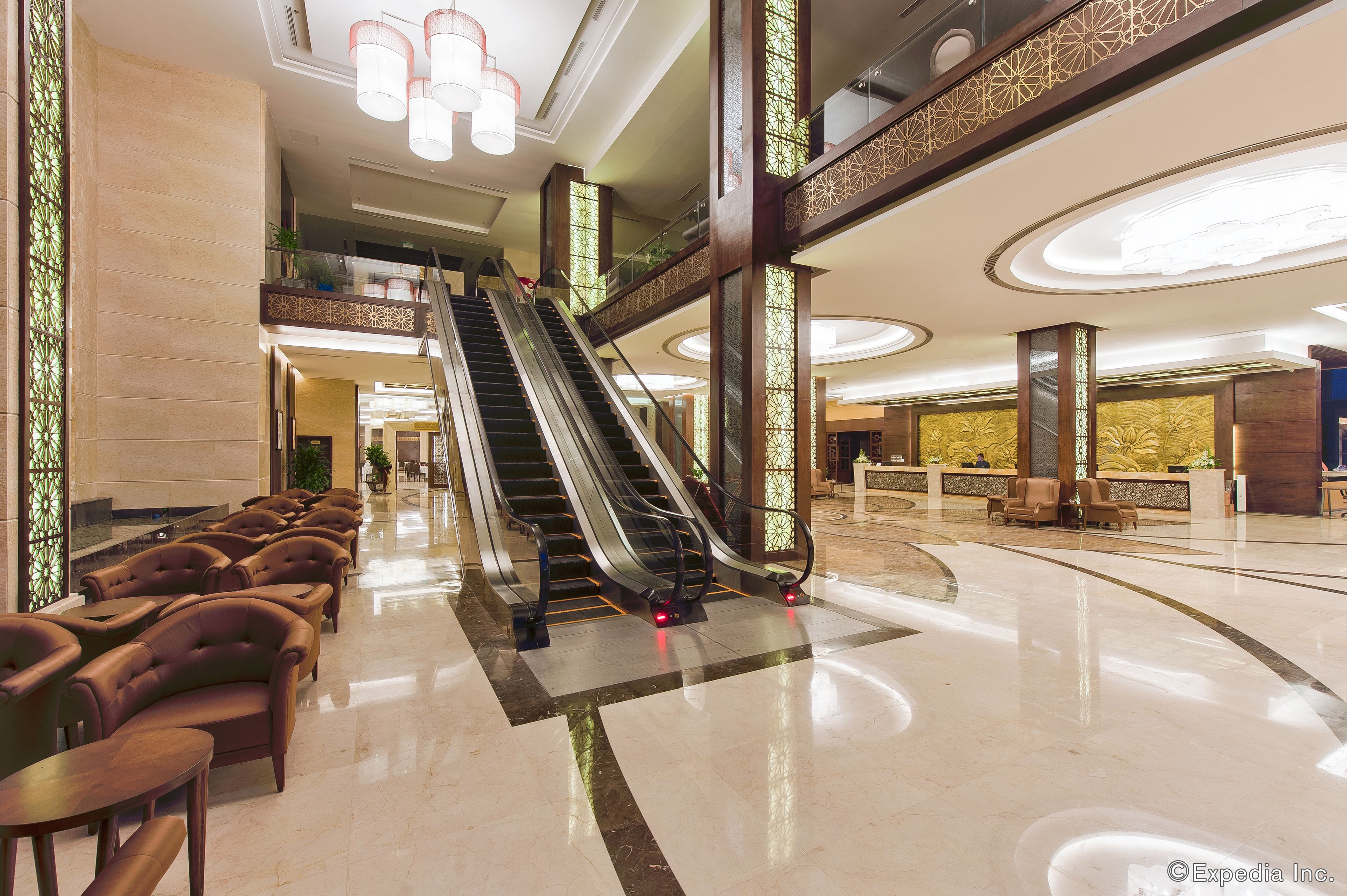 A spacious lobby with a central escalator, seating area with leather chairs, and decorative lighting.