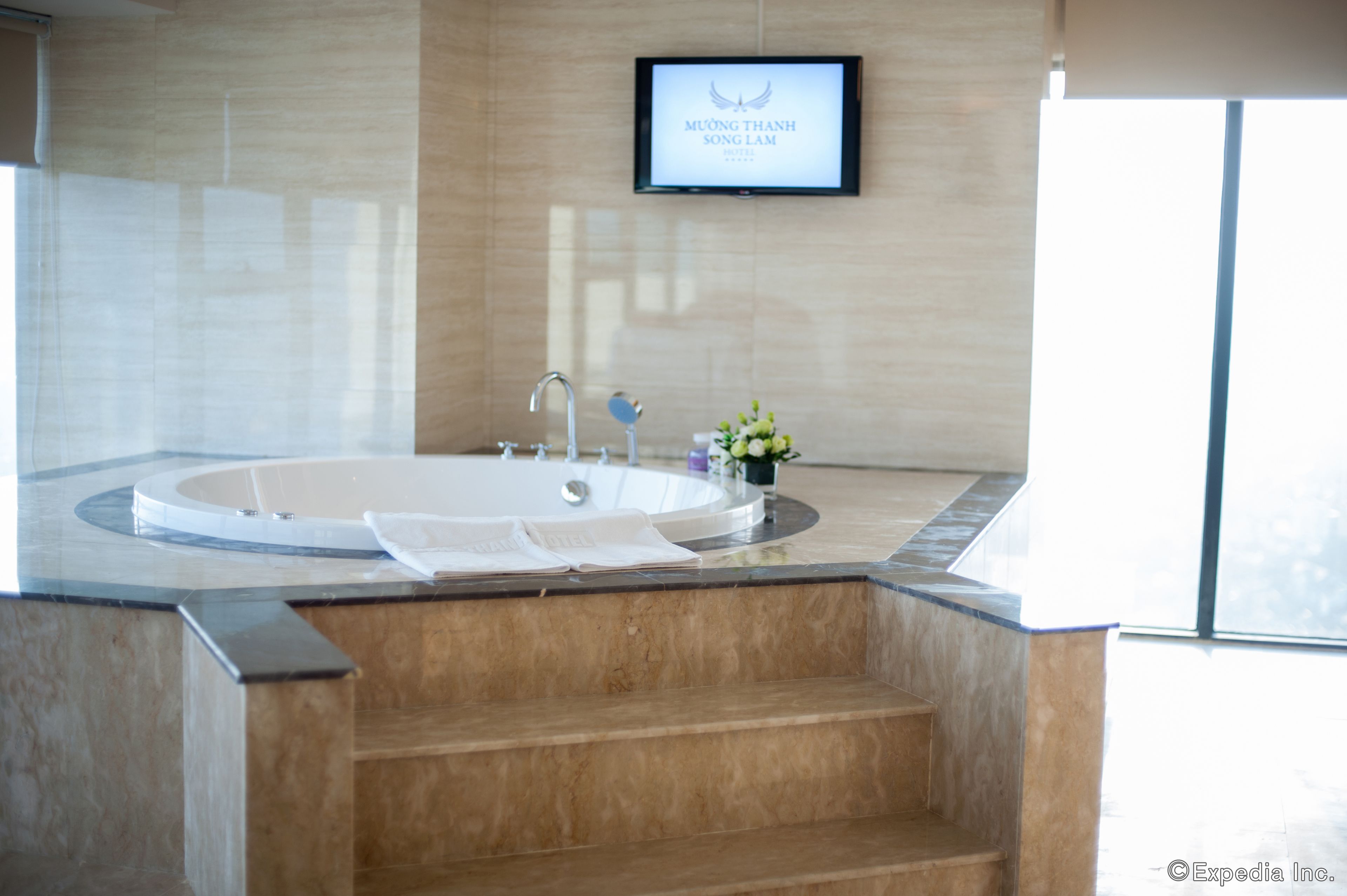 Un bany modern amb una banyera gran, un lavabo i un televisor fixat a la paret que mostra un logotip.