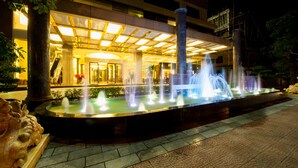 A nighttime view of a hotel with a fountain, a covered entrance, and a staircase.