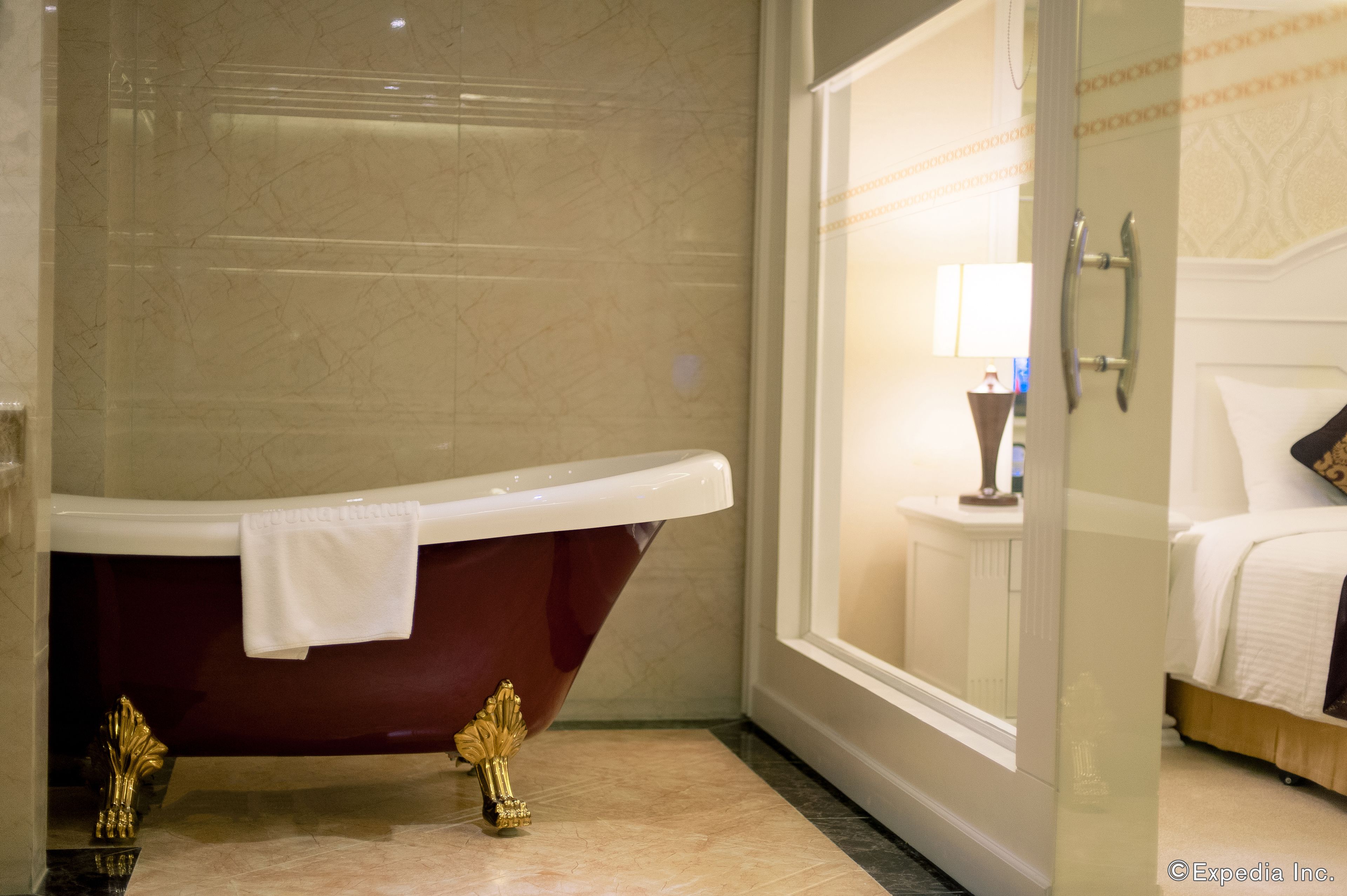 A bathroom with a freestanding bathtub, a glass shower enclosure, and a bed with a white headboard.