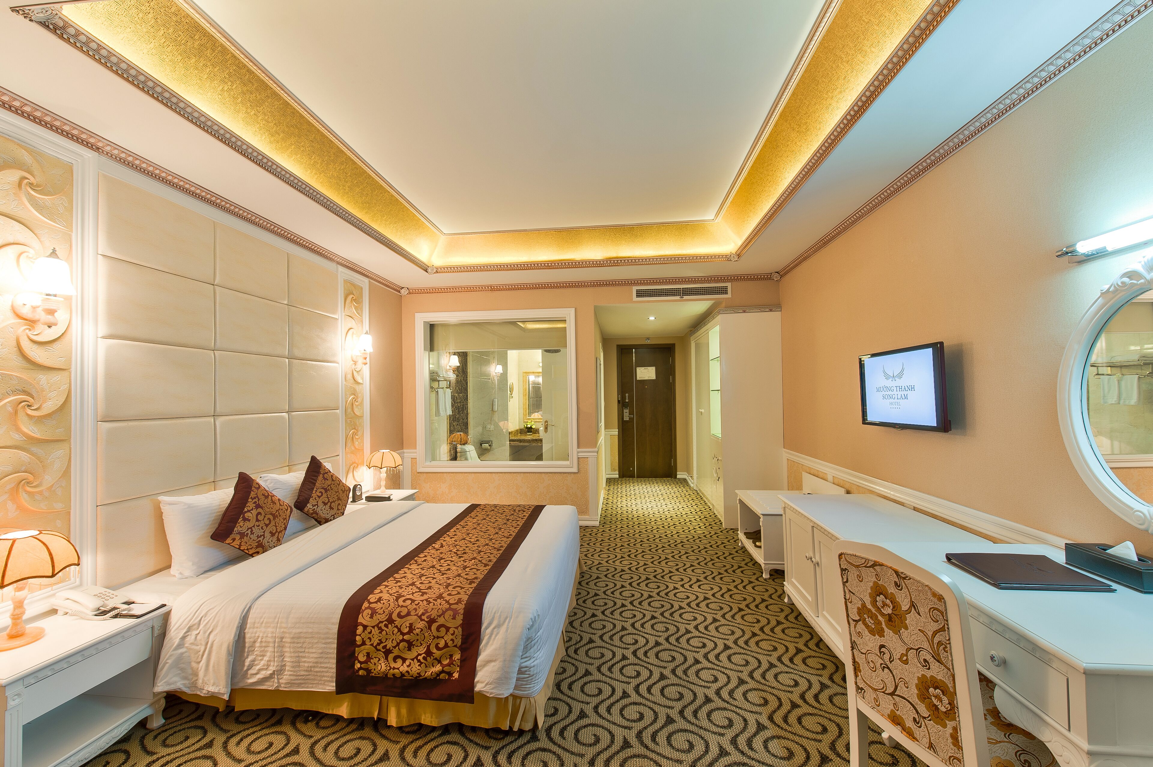 A hotel room with a large bed, bedside tables, a desk, a mirror, and a television.