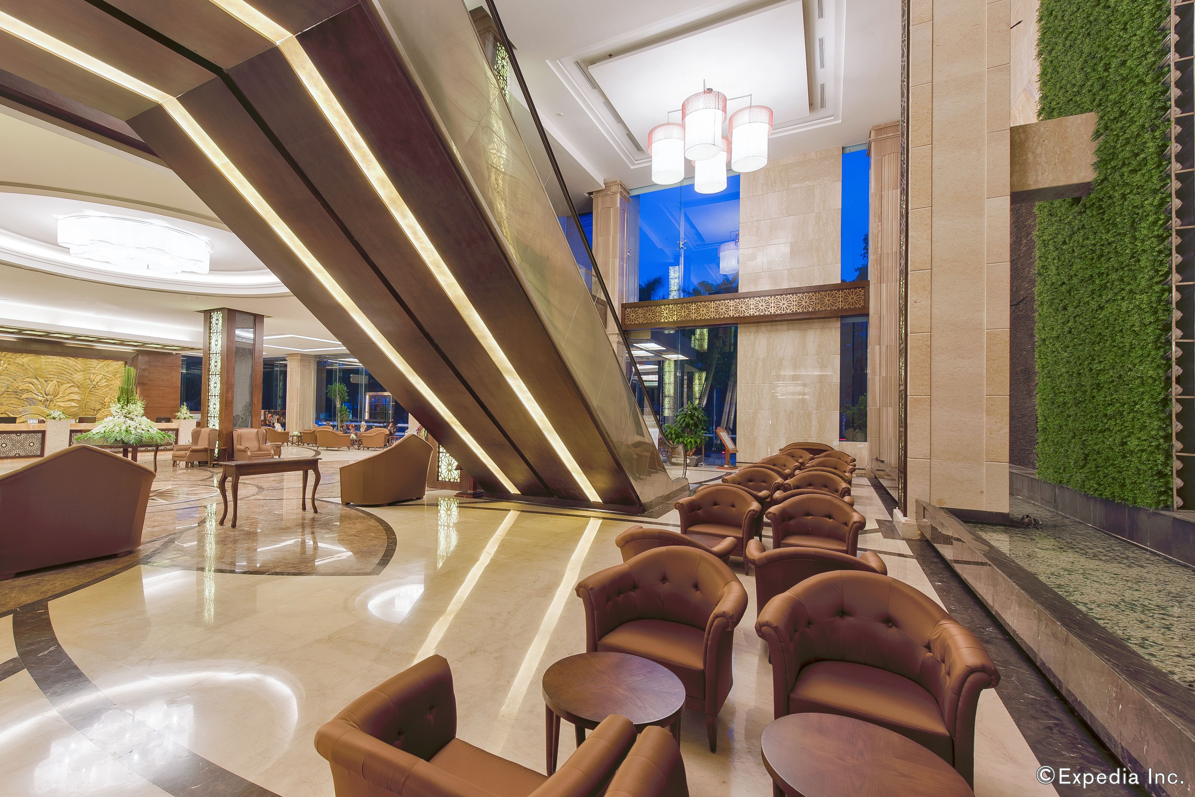 A modern lobby with a central staircase, seating area, and a green wall feature.