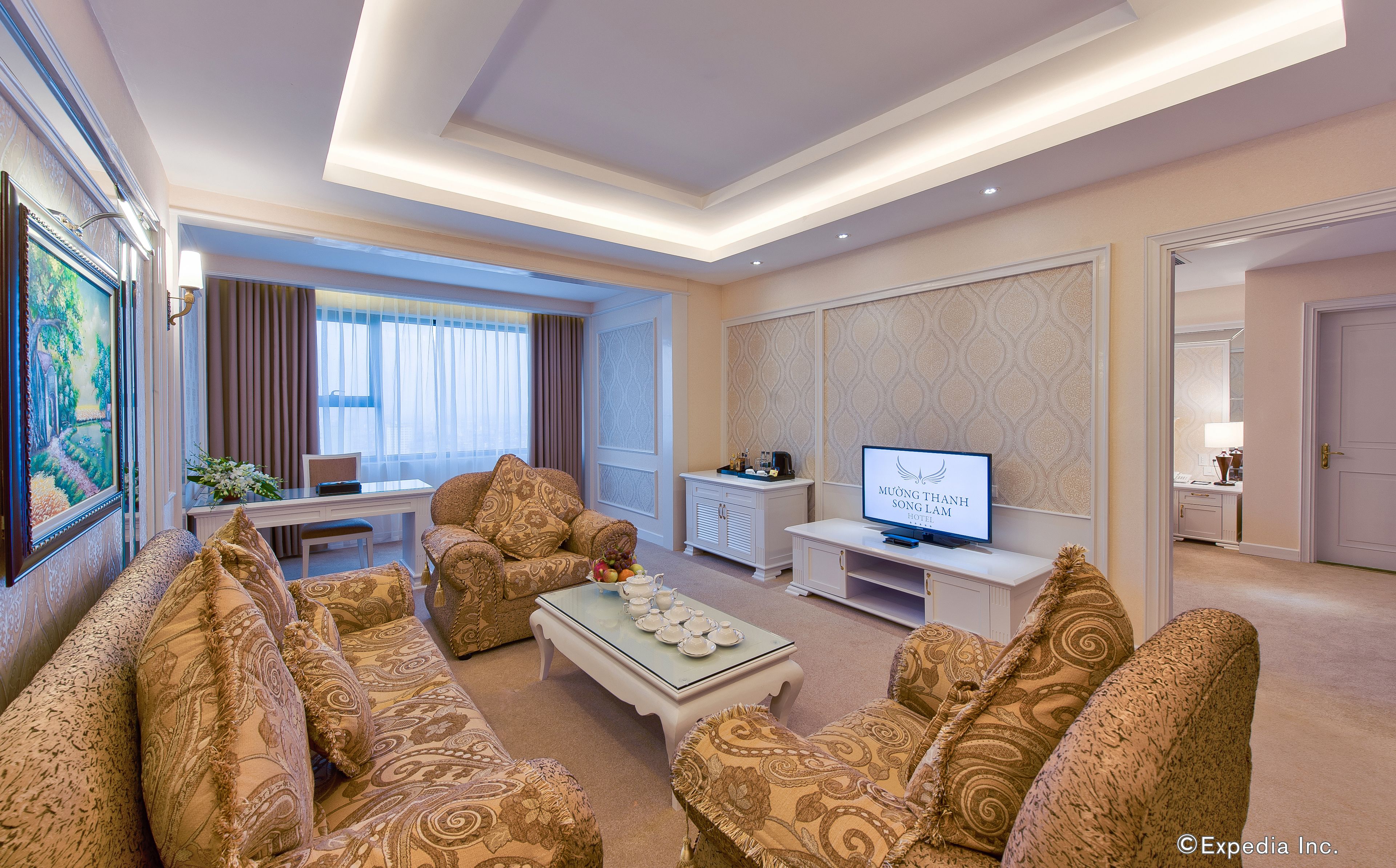 A hotel living room with a sofa set, a coffee table, a TV, and a desk with a computer.