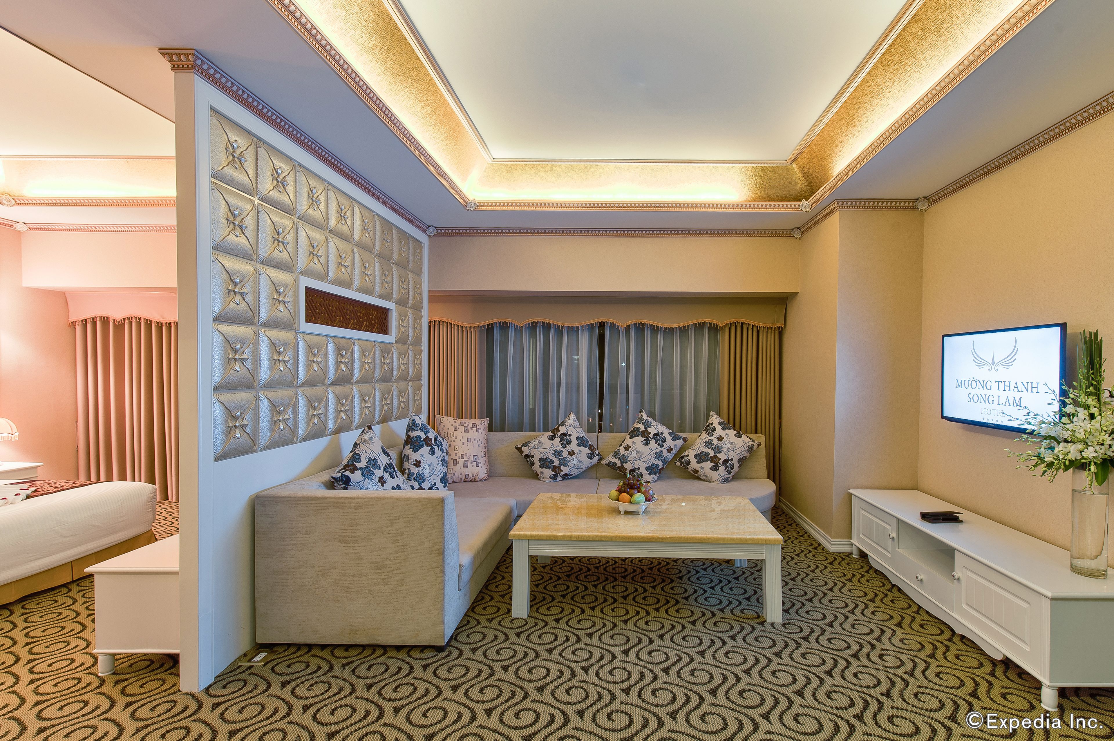 A modern hotel room with a sofa set, a coffee table, a TV, and a patterned carpet.