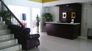 A reception area with a dark reception desk, a staircase with black railings, and a potted plant. - SofyanInn Srigunting (Bogor)