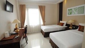 A hotel room with two single beds, a desk with a lamp, a TV, and a window with curtains. - SofyanInn Srigunting (Bogor)