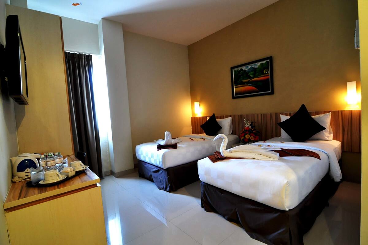 A hotel room with two beds, a desk with a tray of breakfast items, a television, and a painting on the wall.
