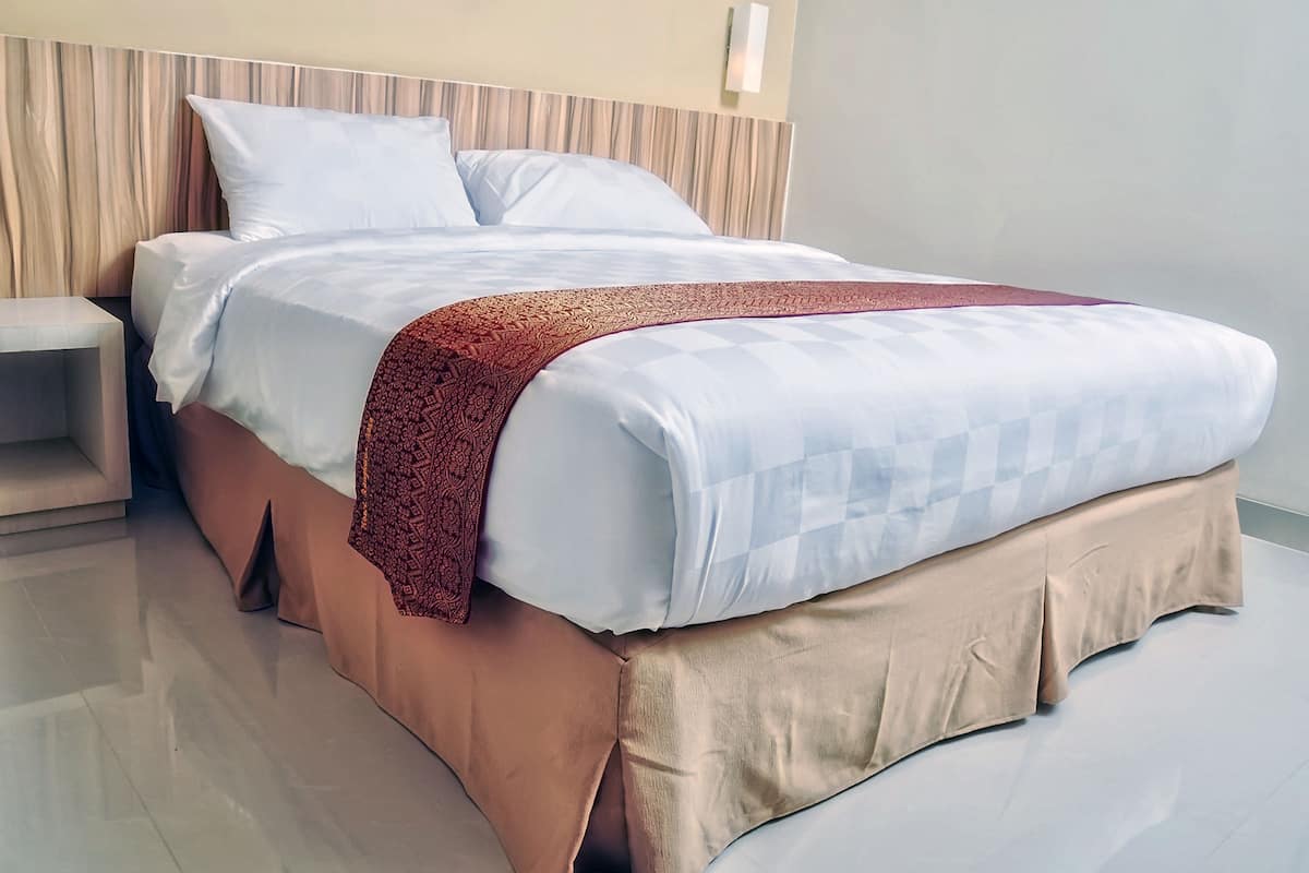 A modern hotel room with a large bed, a nightstand, and a wall-mounted light fixture.