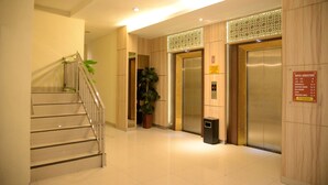A hotel lobby with a staircase, two elevators, a potted plant, and a sign indicating the hotel directory. - Rangkayo Basa Halal Hotel (Padang)