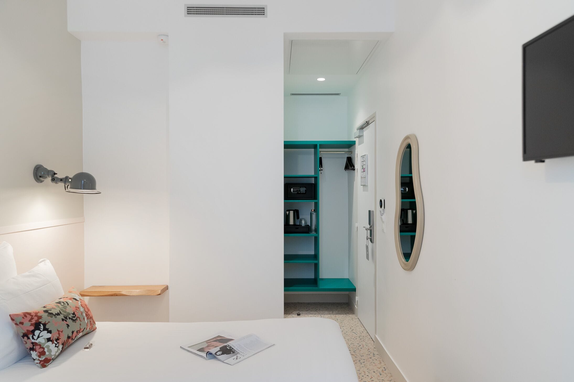 A hotel room with a bed, a nightstand, a wall-mounted TV, a wardrobe, and a small window.