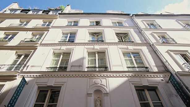 A multi-story building with a classical architectural style, featuring a central entrance with a statue, multiple balconies, and a sign indicating the building's name. - Trendy Canette Hotel (Paris)