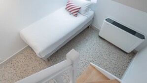 A small, single-bed room with a white bed, a red and white striped pillow, and a white air conditioner against the wall. - Trendy Canette Hotel (Paris)
