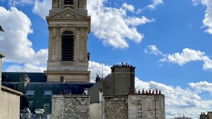 A historic tower with classical architecture, including columns and a balcony, set against a clear blue sky with scattered clouds. - Trendy Canette Hotel (Paris)