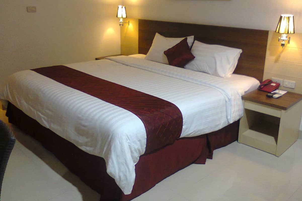 A hotel room with a large bed, two bedside tables, and two wall-mounted lamps.