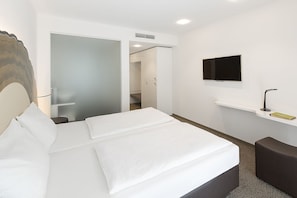 A hotel room with a bed, a TV mounted on the wall, a small table, and a bench.