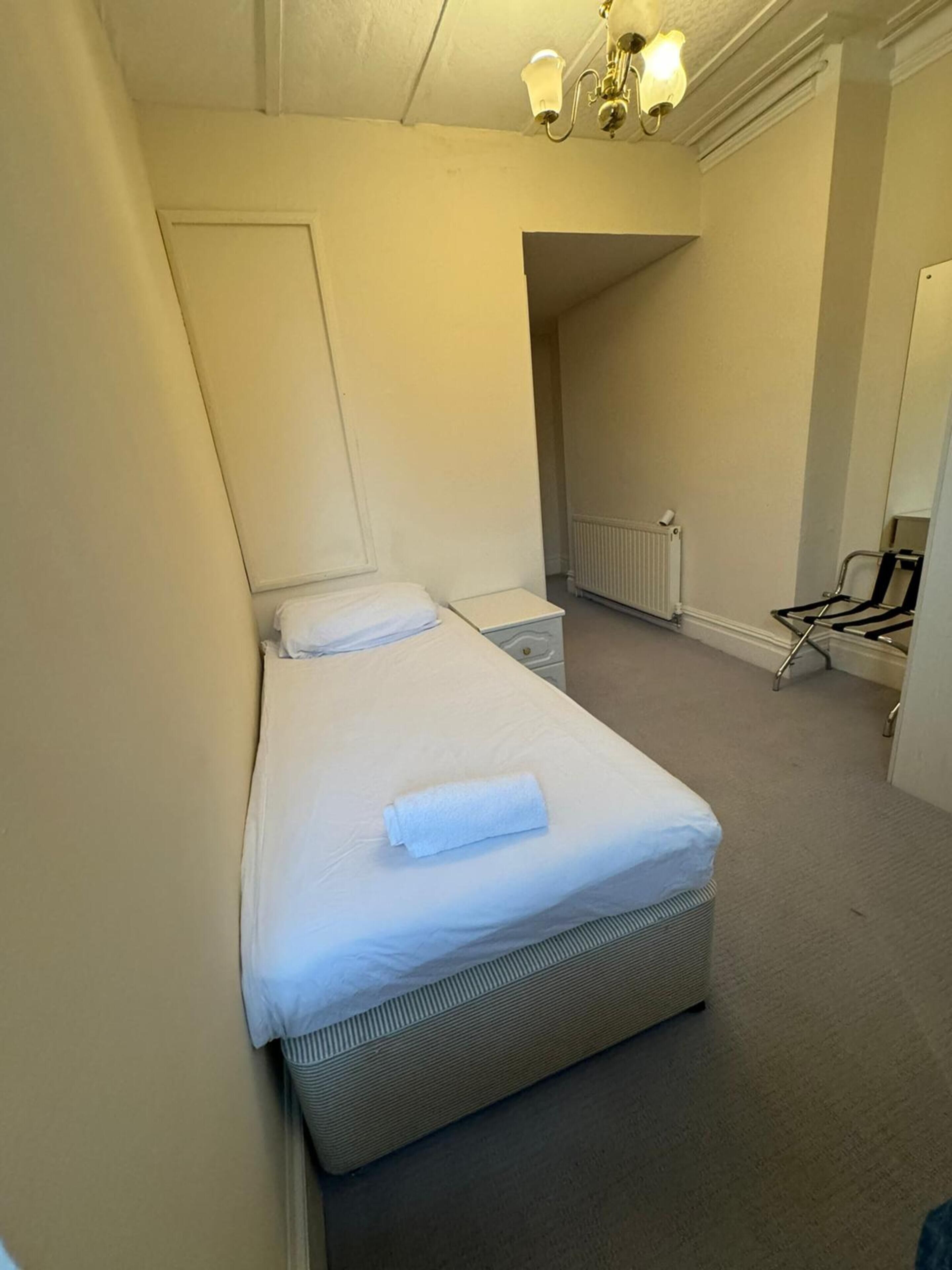 A small, neatly made bed in a compact room with a radiator and a chair.