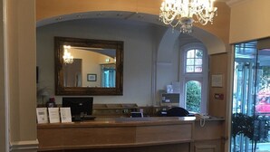 A reception area with a wooden counter, a large mirror, a chandelier, and a glass door leading outside. - Langford Hotel, Brighton & Hove (Hove)