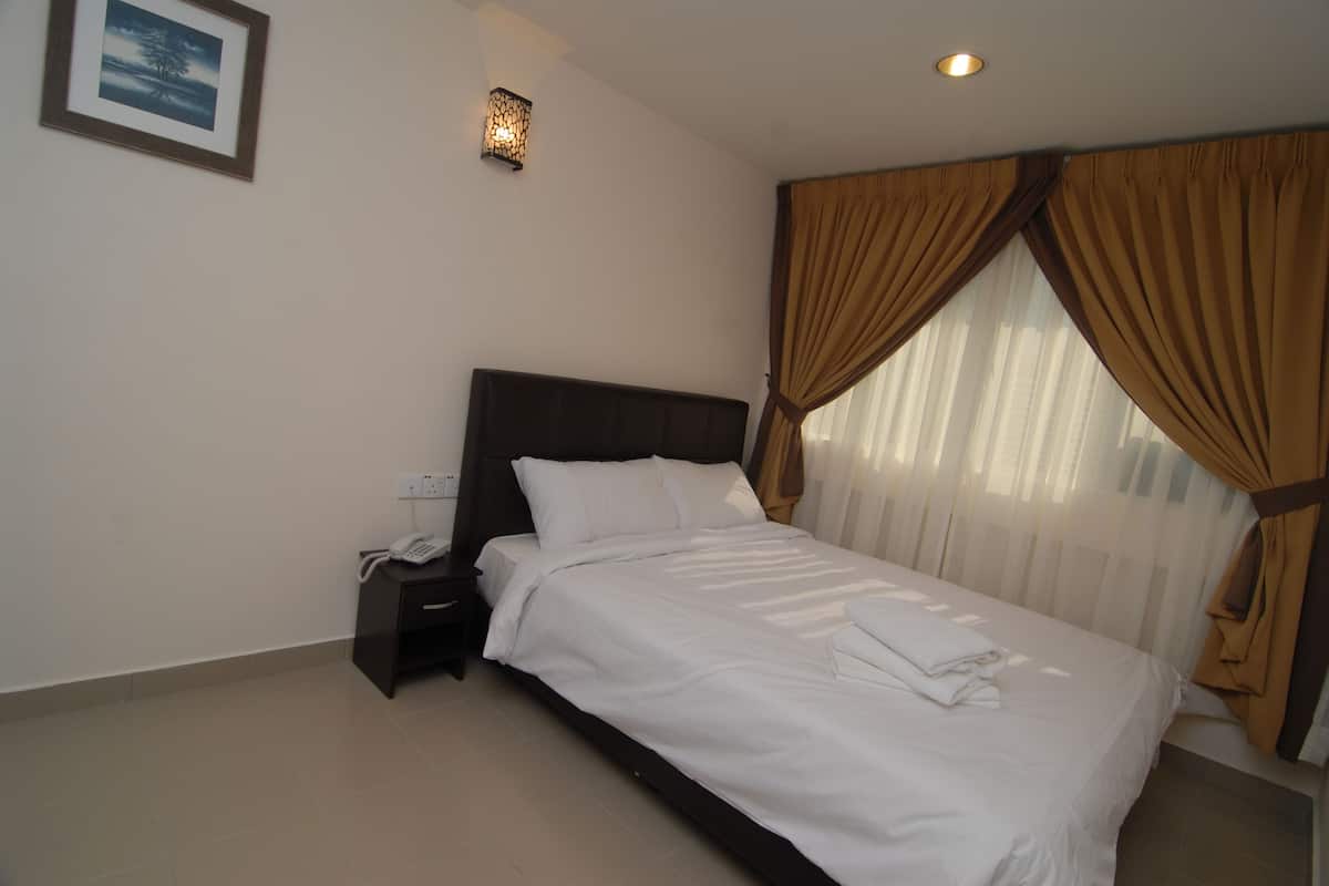 A neatly made bed with white linens, a bedside table with a telephone, and a wall-mounted light fixture.