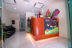 Una recepción de hotel con un mural colorido, un letrero que dice "HOTEL A-ONE" y una planta en el mostrador.