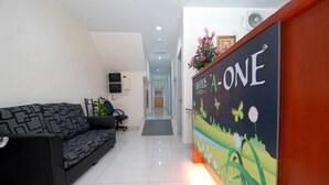 A hotel reception area with a black sofa, a reception desk with a colorful floral design, and a hallway leading to the rooms. - Hotel A-One (Kuala Lumpur)