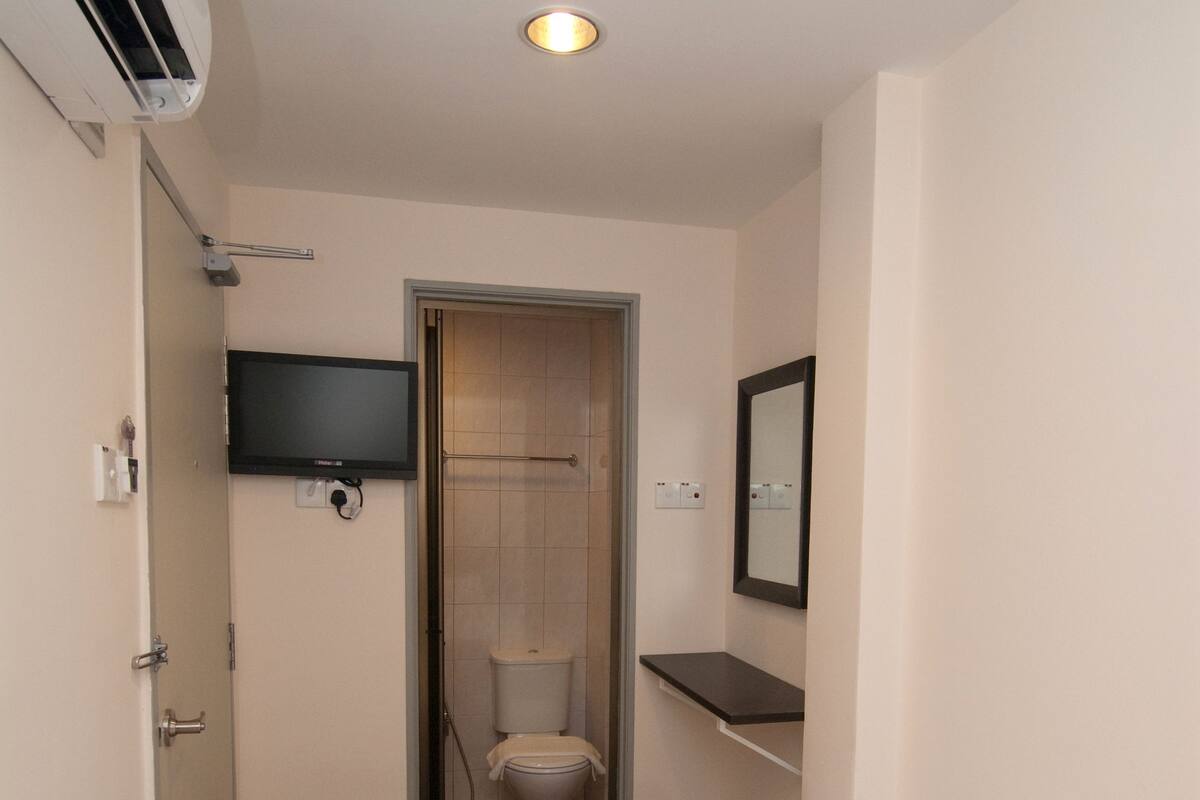 A hotel room with a bed, a television mounted on the wall, a toilet, and a shower area.