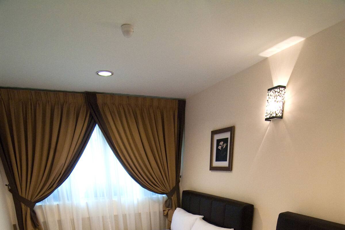 A hotel room with two beds, a nightstand with a phone, a wall-mounted light, and a window with curtains.