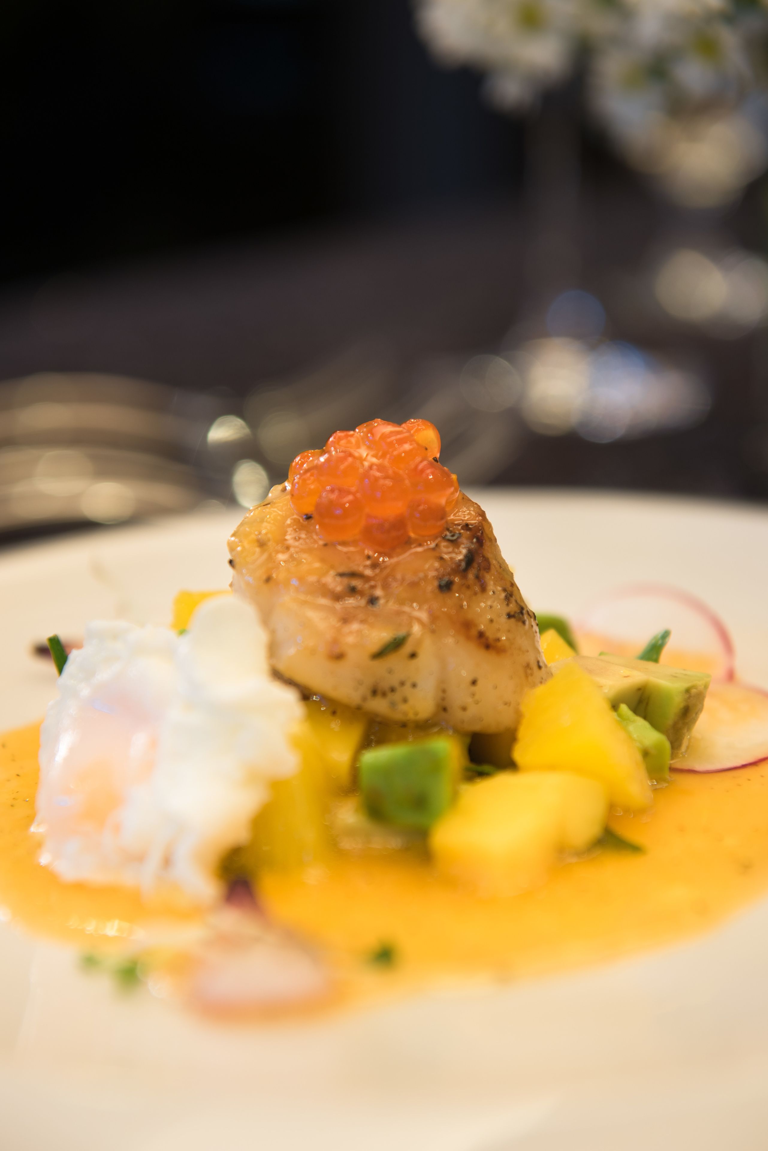 A dish with fish, avocado, mango, and a poached egg on a plate.