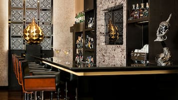A bar area with a long counter, multiple stools, and shelves stocked with bottles.